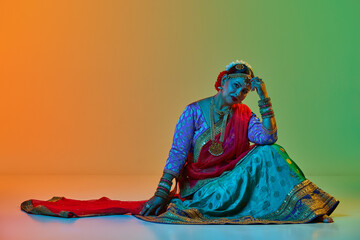 Indian culture. Mature, beautiful indian woman in traditional clothes, dress posing over gradient studio background in neon light. Concept of beauty, fashion, India, traditions, choreography, art. Ad