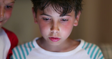 Wall Mural - Boys in front of tablet screen with blue light glowing on face at night. Children watching content online browsing internet