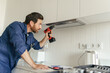 © Daria - Professional male worker in uniform use screwdriver to repairing modern cooker hood in kitchen
