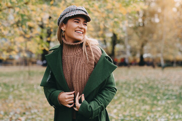 Wall Mural - Joyful girl in warm clothing smiling at public park. Young student girl taking a walk outside of her college campus during the nice autumn day.