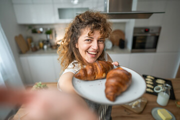 Wall Mural - One adult caucasian woman stand in the kitchen with fresh croissant