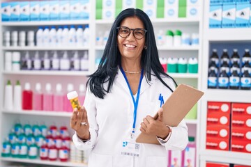 Wall Mural - Middle age hispanic woman pharmacist holding pills bottle reading document at pharmacy