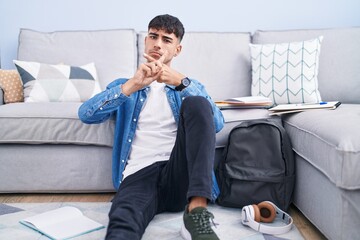 Wall Mural - Young hispanic man sitting on the floor studying for university rejection expression crossing fingers doing negative sign