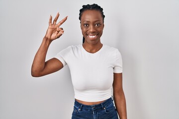 Wall Mural - Beautiful black woman standing over isolated background smiling positive doing ok sign with hand and fingers. successful expression.