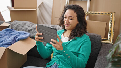 Poster - Young beautiful hispanic woman using touchpad sitting on sofa at new home