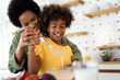 © Dorde - Playful African American family preparing food with wire whisk at home.