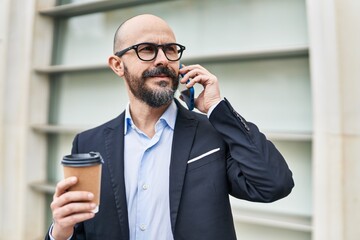 Canvas Print - Young bald man business worker talking on smartphone drinking coffee at street