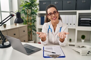 Poster - Young hispanic woman wearing doctor uniform and stethoscope smiling cheerful offering hands giving assistance and acceptance.