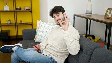 Canvas Print - Young hispanic man using smartphone doing ok gesture at home