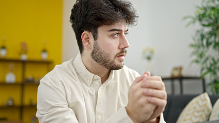 Poster - Young hispanic man sitting on sofa with serious expression at home