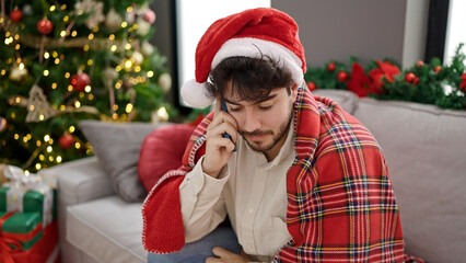 Wall Mural - Young hispanic man celebrating christmas talking on smartphone at home