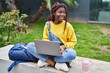 © Krakenimages.com - African american woman student using laptop sitting on bench at campus park