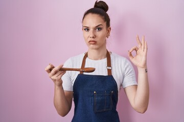 Poster - Young hispanic girl wearing professional cook apron holding wood spoon skeptic and nervous, frowning upset because of problem. negative person.