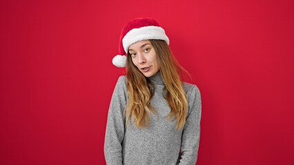 Young caucasian woman wearing christmas hat with serious expression over isolated red background