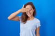 © Krakenimages.com - Brunette woman standing over blue background smiling and laughing with hand on face covering eyes for surprise. blind concept.