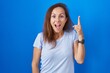 © Krakenimages.com - Brunette woman standing over blue background pointing finger up with successful idea. exited and happy. number one.