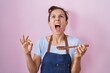 © Krakenimages.com - Brunette woman wearing professional cook apron holding wooden spoon angry and mad screaming frustrated and furious, shouting with anger looking up.