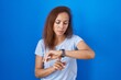© Krakenimages.com - Brunette woman standing over blue background checking the time on wrist watch, relaxed and confident