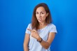 © Krakenimages.com - Brunette woman standing over blue background pointing aside worried and nervous with forefinger, concerned and surprised expression