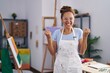 © Krakenimages.com - Brunette woman painting at art studio screaming proud, celebrating victory and success very excited with raised arms