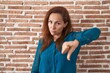 © Krakenimages.com - Brunette woman standing over bricks wall looking unhappy and angry showing rejection and negative with thumbs down gesture. bad expression.