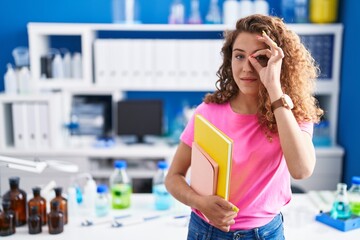 Poster - Young caucasian student woman at scientist laboratory smiling happy doing ok sign with hand on eye looking through fingers