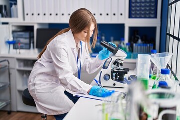 Wall Mural - Young caucasian woman scientist using microscope write on document at laboratory