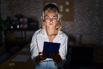 Poster - Young blonde woman working at the office at night skeptic and nervous, frowning upset because of problem. negative person.