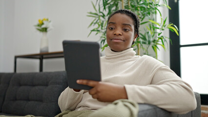 Poster - African american woman using touchpad sitting on sofa at home