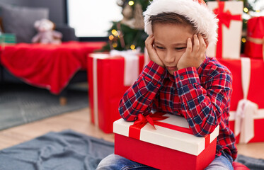 Canvas Print - Adorable hispanic boy holding christmas gift sitting on floor with unhappy expression at home