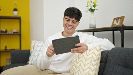 Poster - Young hispanic man using touchpad sitting on sofa at home