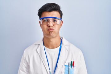 Canvas Print - Hispanic man working as scientist puffing cheeks with funny face. mouth inflated with air, crazy expression.