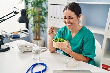 Canvas Print - Young beautiful hispanic woman doctor smiling confident eating salad at clinic