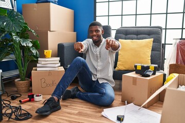 Canvas Print - African american man sitting on the floor at new home pointing to you and the camera with fingers, smiling positive and cheerful