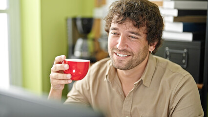 Canvas Print - Young hispanic man business worker using computer drinking coffee at office