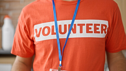 Wall Mural - Young hispanic man wearing volunteer uniform standing at charity center