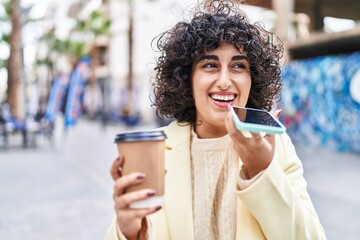 Wall Mural - Young middle east woman excutive talking on the smartphone drinking coffee at street