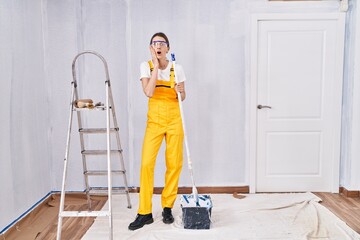 Poster - Young caucasian woman painting walls afraid and shocked, surprise and amazed expression with hands on face