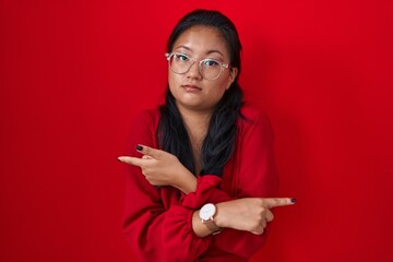 Sticker - Asian young woman standing over red background pointing to both sides with fingers, different direction disagree