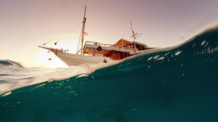 Wall Mural - Liveaboard boat anchored in the bay. Splitted underwater view during sunset. The Komodo National Park, Indonesia