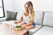 © Krakenimages.com - Young woman eating salad sitting on sofa at home
