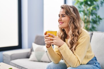 Poster - Young woman drinking coffee sitting on sofa at home