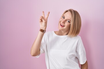 Poster - Young caucasian woman standing over pink background smiling looking to the camera showing fingers doing victory sign. number two.