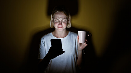 Wall Mural - Young blonde woman using smartphone holding cup of coffee tired over isolated yellow background