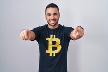 Young Hispanic Man Wearing Bitcoin T Shirt Pointing To You And The Camera With Fingers, Smiling Positive And Cheerful