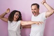 Middle age hispanic couple together over pink background dancing happy and cheerful, smiling moving casual and confident listening to music