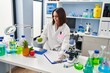 © Krakenimages.com - Young beautiful hispanic woman scientist holding apple writing on document at laboratory