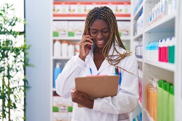 Poster - African american woman pharmacist talking on smartphone reading document at pharmacy