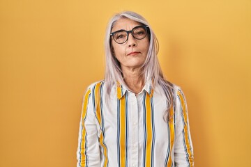 Wall Mural - Middle age woman with grey hair standing over yellow background wearing glasses relaxed with serious expression on face. simple and natural looking at the camera.