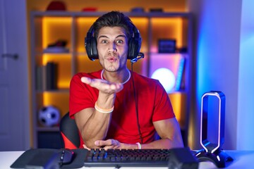 Wall Mural - Young hispanic man playing video games looking at the camera blowing a kiss with hand on air being lovely and sexy. love expression.